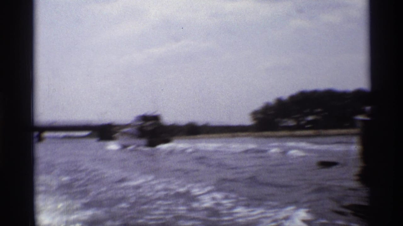 A wide 8mm view shows a small motorboat crossing open river water with shoreline trees in the distance.