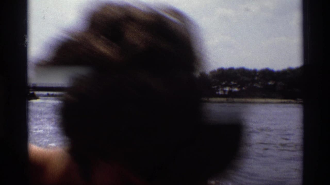 Young man in close foreground beside lake water with a distant shoreline.