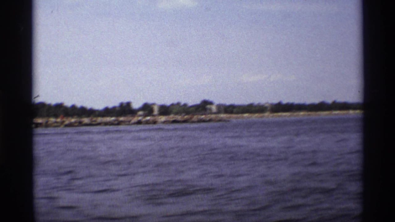 1973 New York 8mm frame showing a low shoreline across the water, divided by dark boat-window or railing edges.