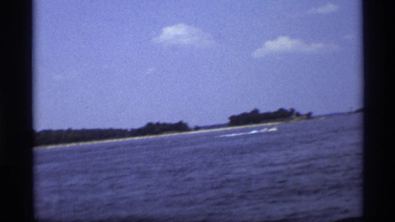 Small speedboat crosses near a distant wooded shore, leaving a white wake.