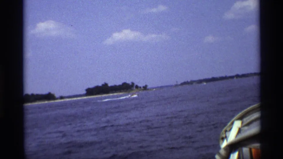 1973 New York 8mm frame showing a speedboat near the shoreline, with a partial foreground boat edge from the filming position.