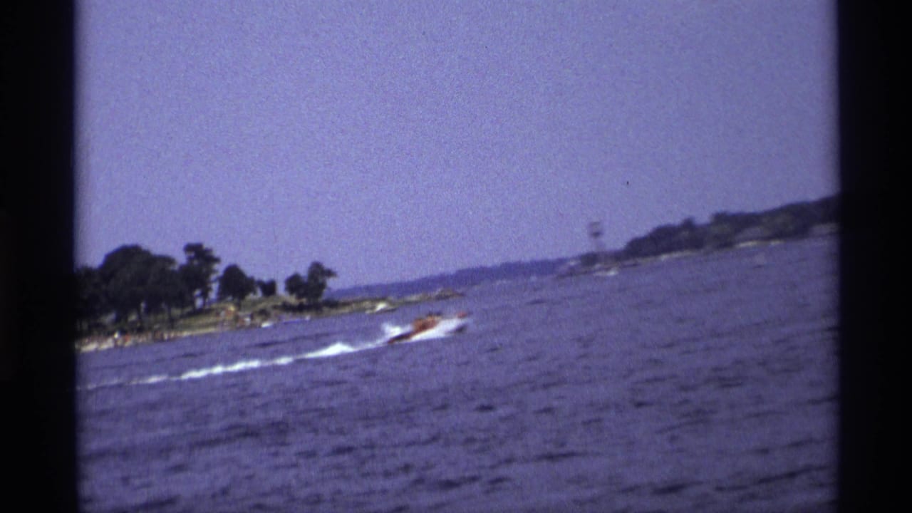 Small motorboat speeding across open water near a tree-lined shore.