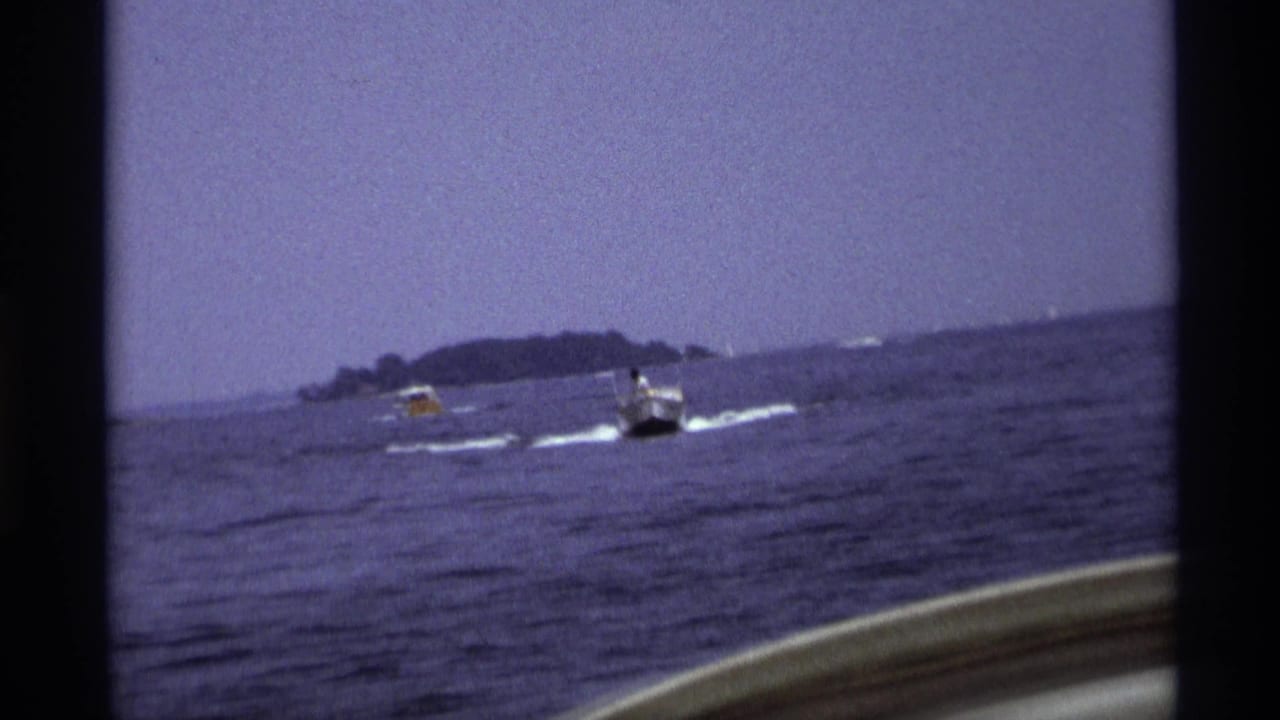 White motorboat and smaller yellow craft moving across rippled water near an island.