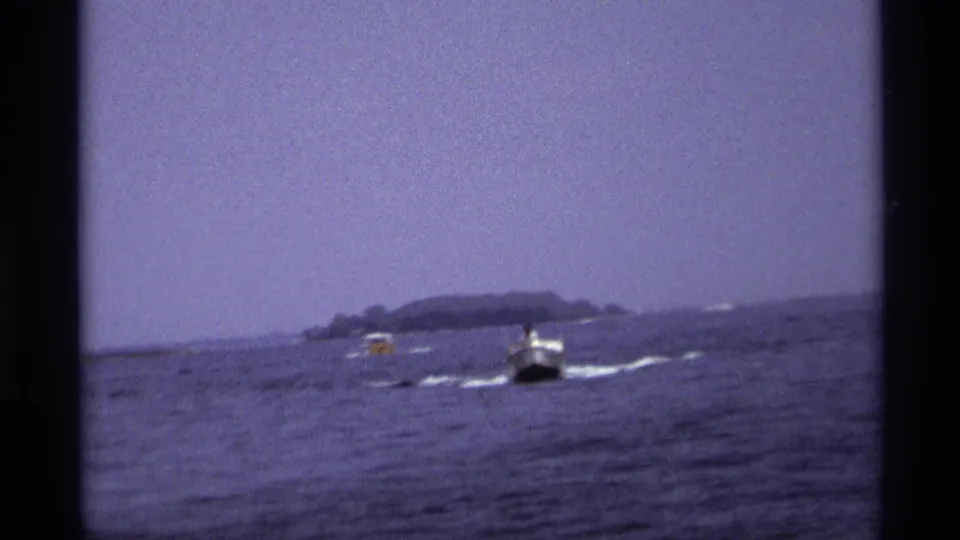 Two small motorboats leave pale wakes across open water, with a low island visible beyond them.