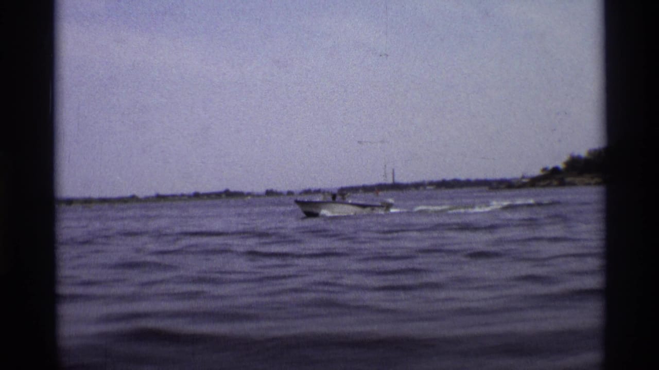 Motorboat farther right on the water, leaving a wake near the distant shoreline.