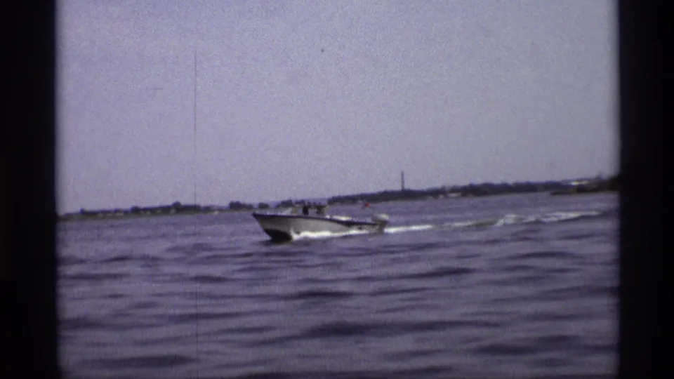 1973 New York 8mm frame with a small recreational boat crossing choppy water, viewed against a distant shoreline.