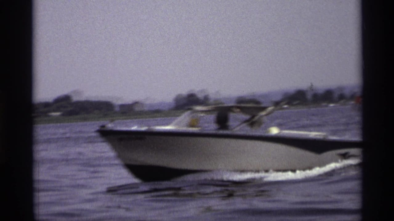 Motorboat passing close to the camera with water and shoreline behind it.