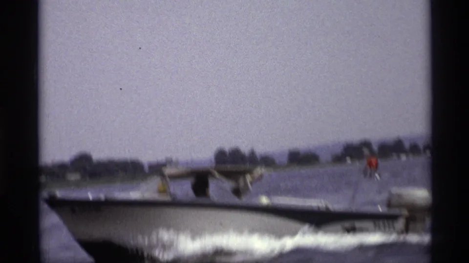 A close, motion-blurred 8mm view shows the white and blue motorboat moving quickly across a New York lake in 1973.