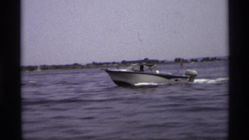1973 New York 8mm frame of a blue and white motorboat moving across open water with a hazy shoreline in the distance.