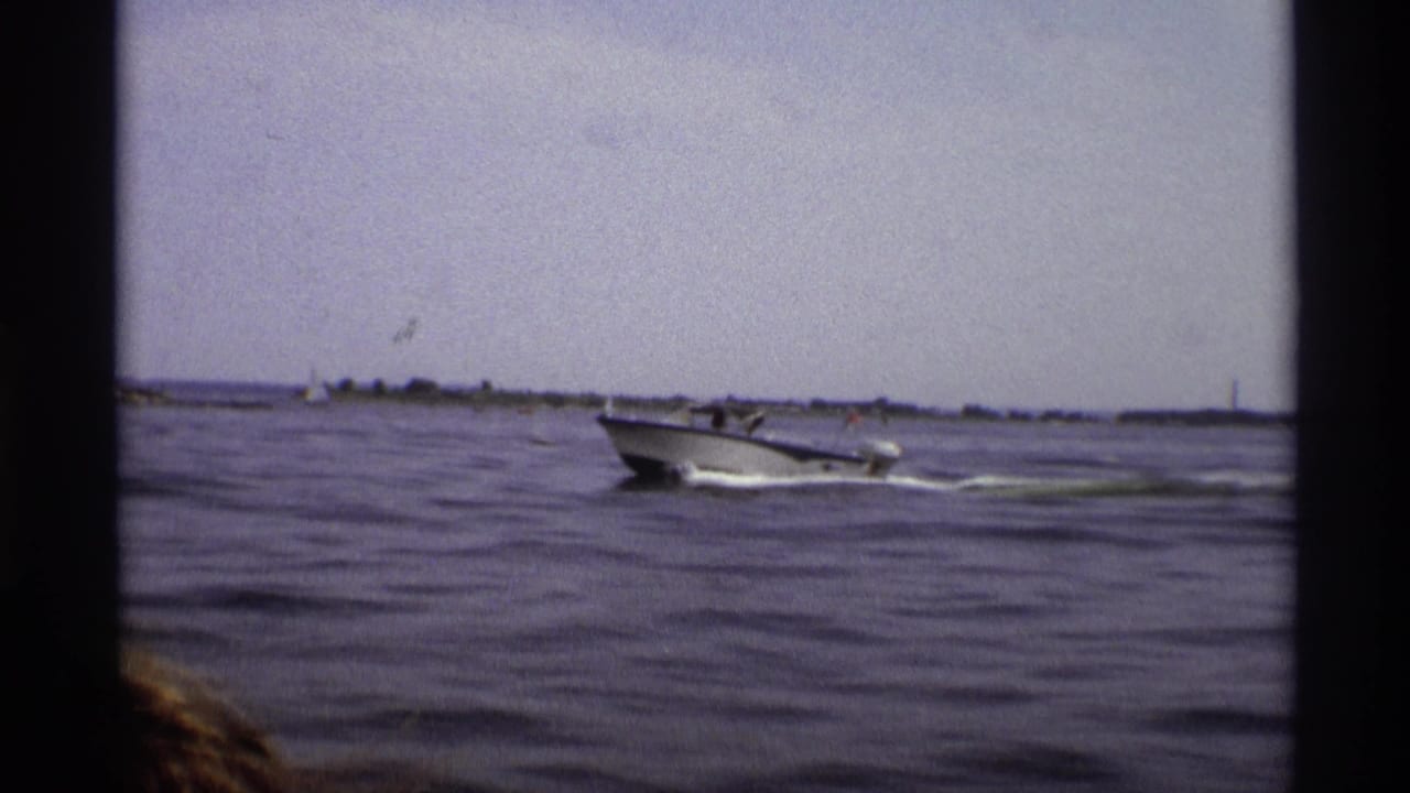 A 1973 New York 8mm frame captures the motorboat crossing open water, with wake, shoreline and film edge visible.