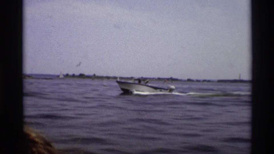 A 1973 New York 8mm frame captures the motorboat crossing open water, with wake, shoreline and film edge visible.