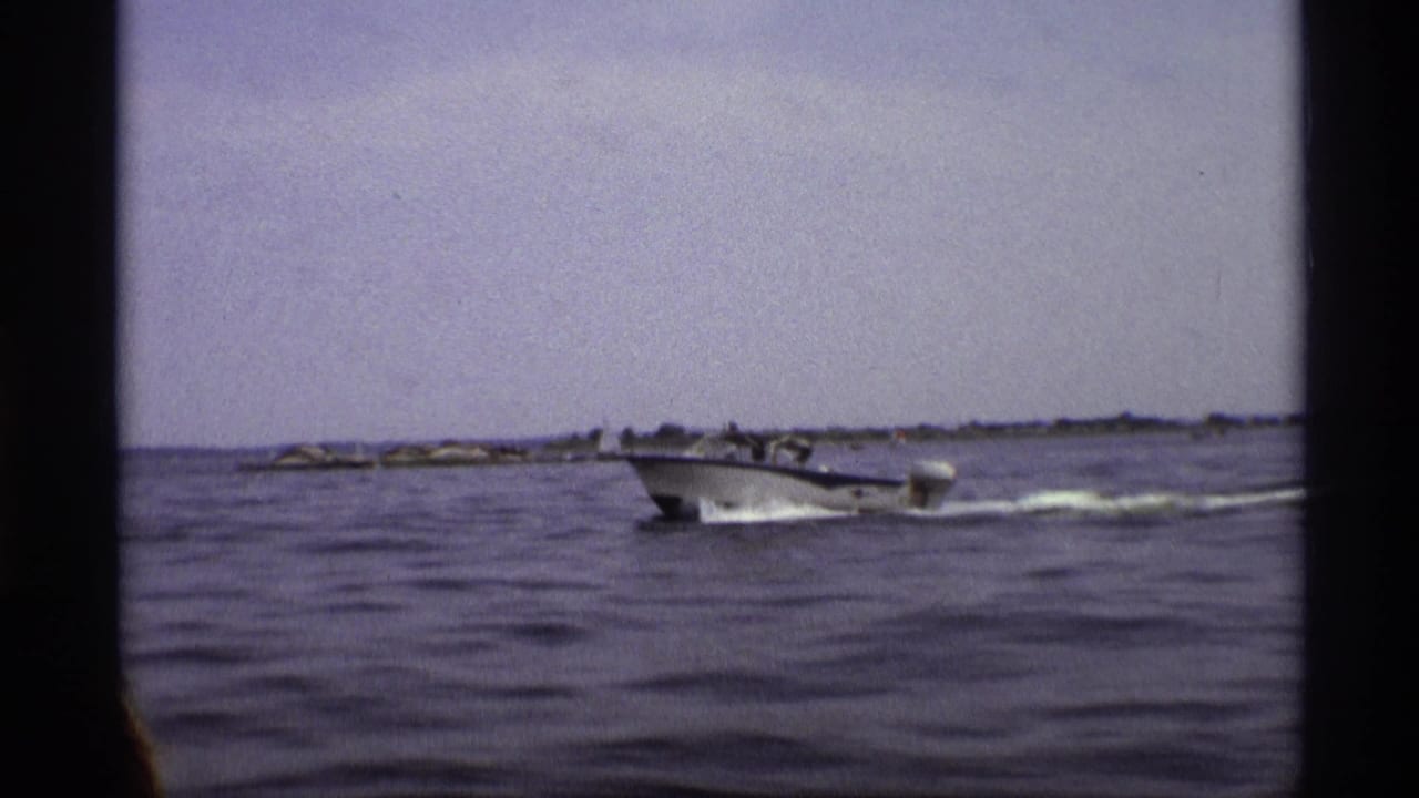 A 1973 New York 8mm frame shows a white motorboat crossing calm water with a faint shoreline behind it.