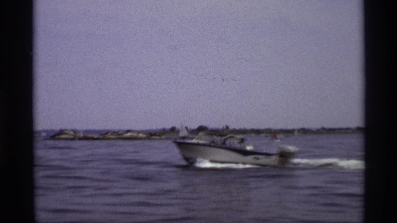 The motorboat angles across the frame on New York waters, with a low shoreline and dark 8mm gate borders visible.