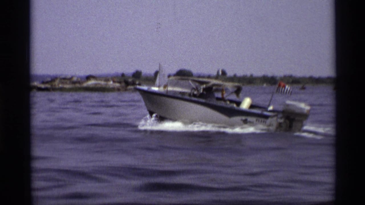 A closer 1973 New York frame shows the motorboat passing with a canopy, outboard motor, wake, and small American flag at the stern.