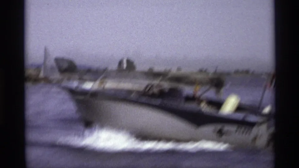 1973 New York home-movie frame showing a blue-and-white speedboat moving across open water near a distant shoreline.