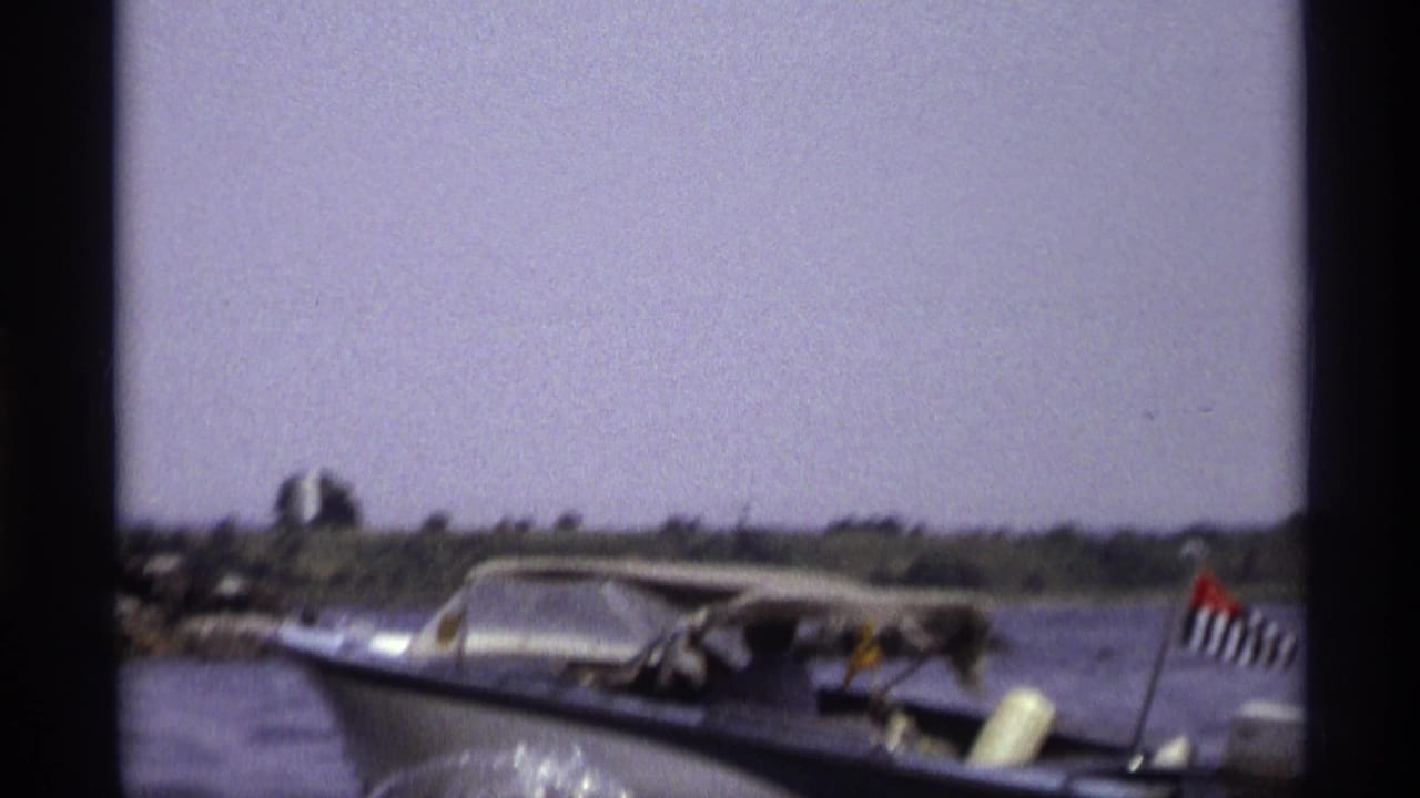 1973 New York frame of a blue-and-white speedboat with visible occupants and a small stern flag on open water.