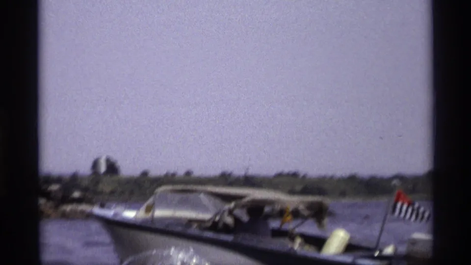 1973 New York frame of a blue-and-white speedboat with visible occupants and a small stern flag on open water.