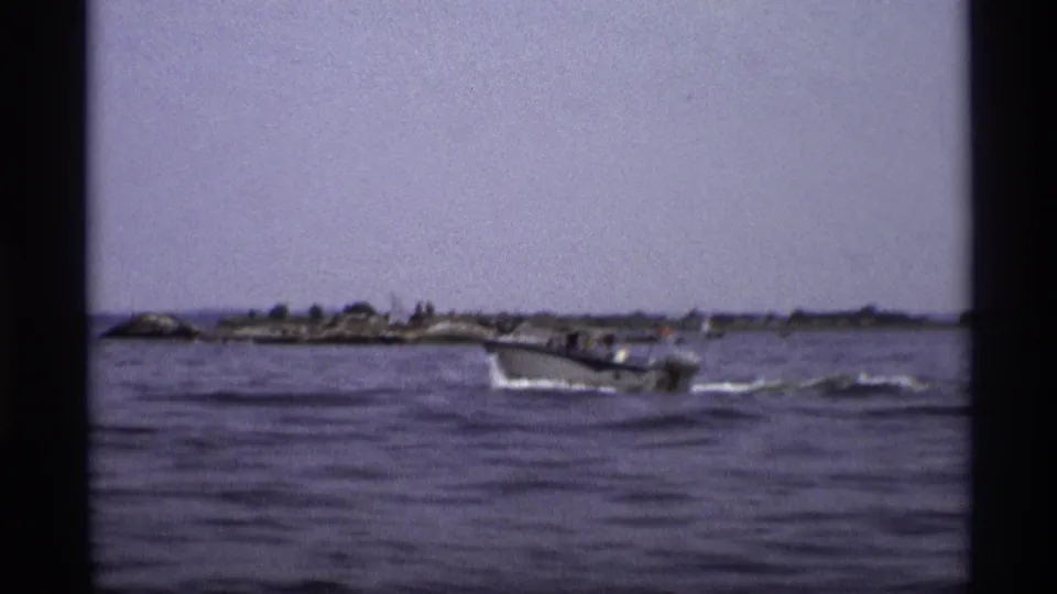 Wide 1973 New York frame with the speedboat farther from camera on open water near a low shoreline.