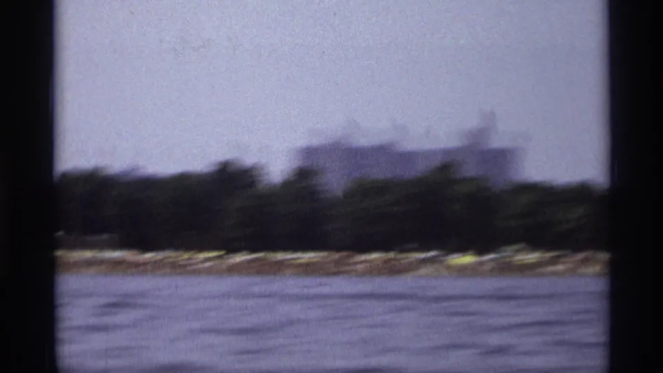 Moving 1973 New York boat footage with blurred water, shoreline trees, and a low building in the distance.