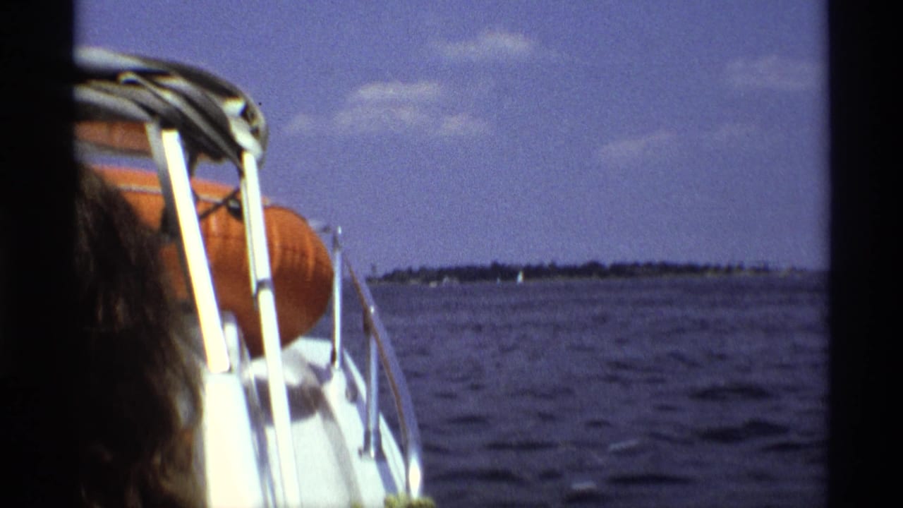 1973 New York home-movie view from a speedboat with white railings, an orange life preserver, and a partial passenger beside open water.