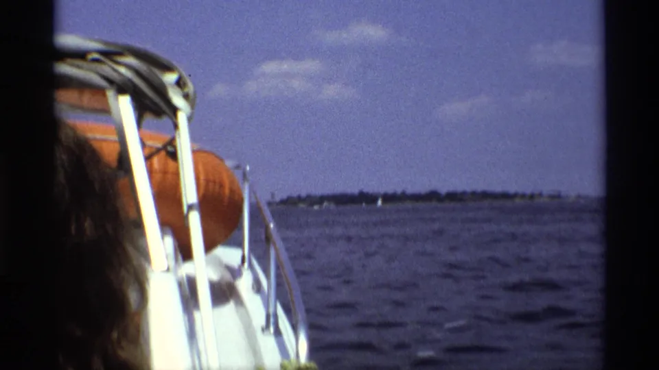 1973 New York home-movie view from a speedboat with white railings, an orange life preserver, and a partial passenger beside open water.