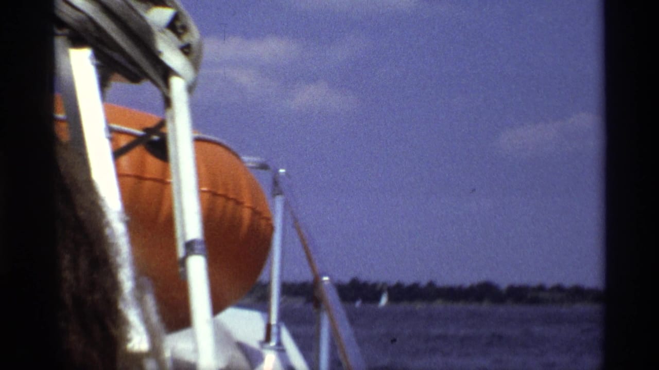 1973 New York speedboat view with close boat railings, an orange life preserver, choppy water, and a low distant shoreline.