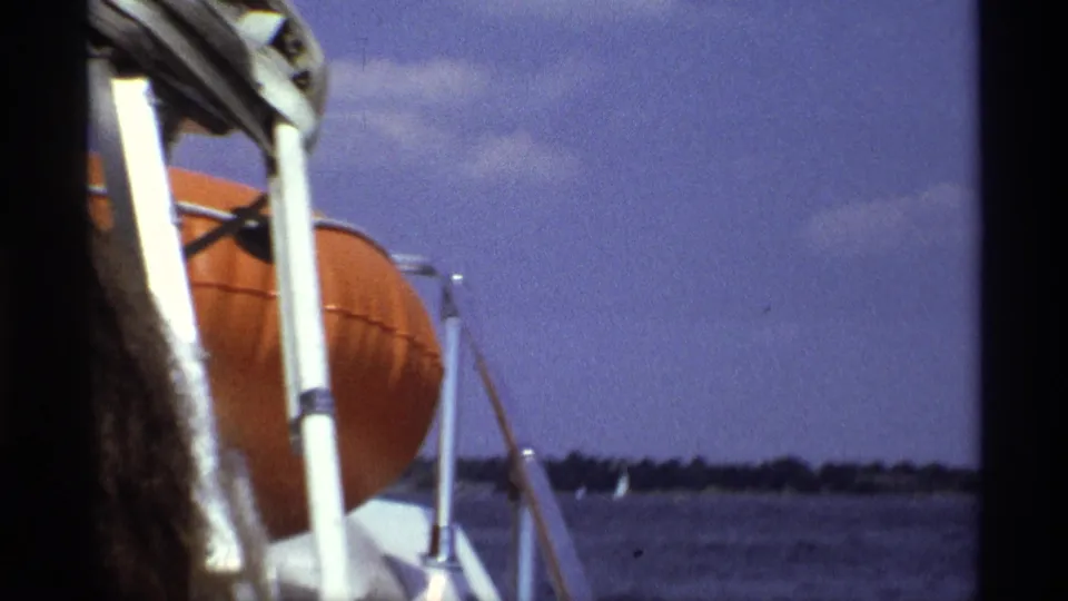 1973 New York speedboat view with close boat railings, an orange life preserver, choppy water, and a low distant shoreline.