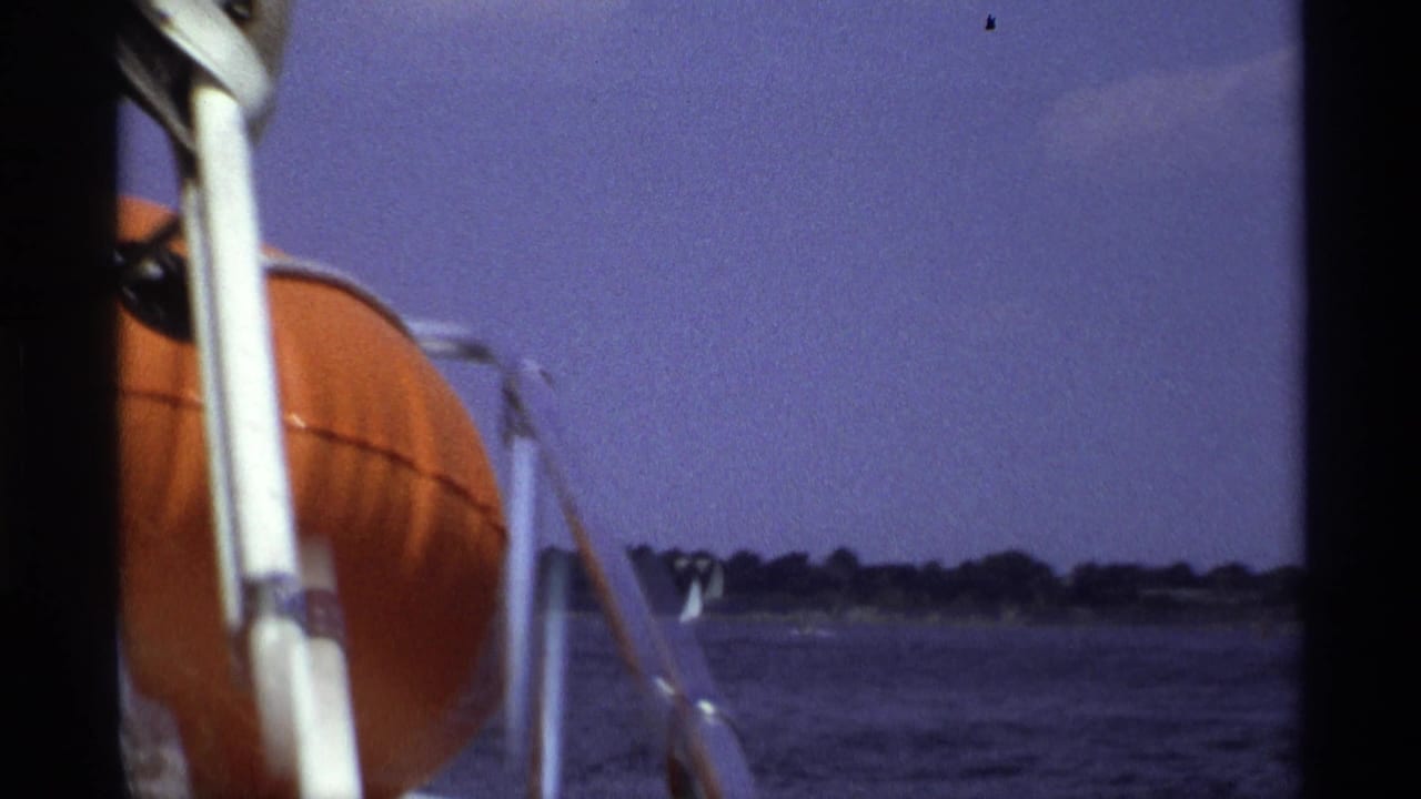 Boat railings and orange life preserver beside open water and a distant shoreline.