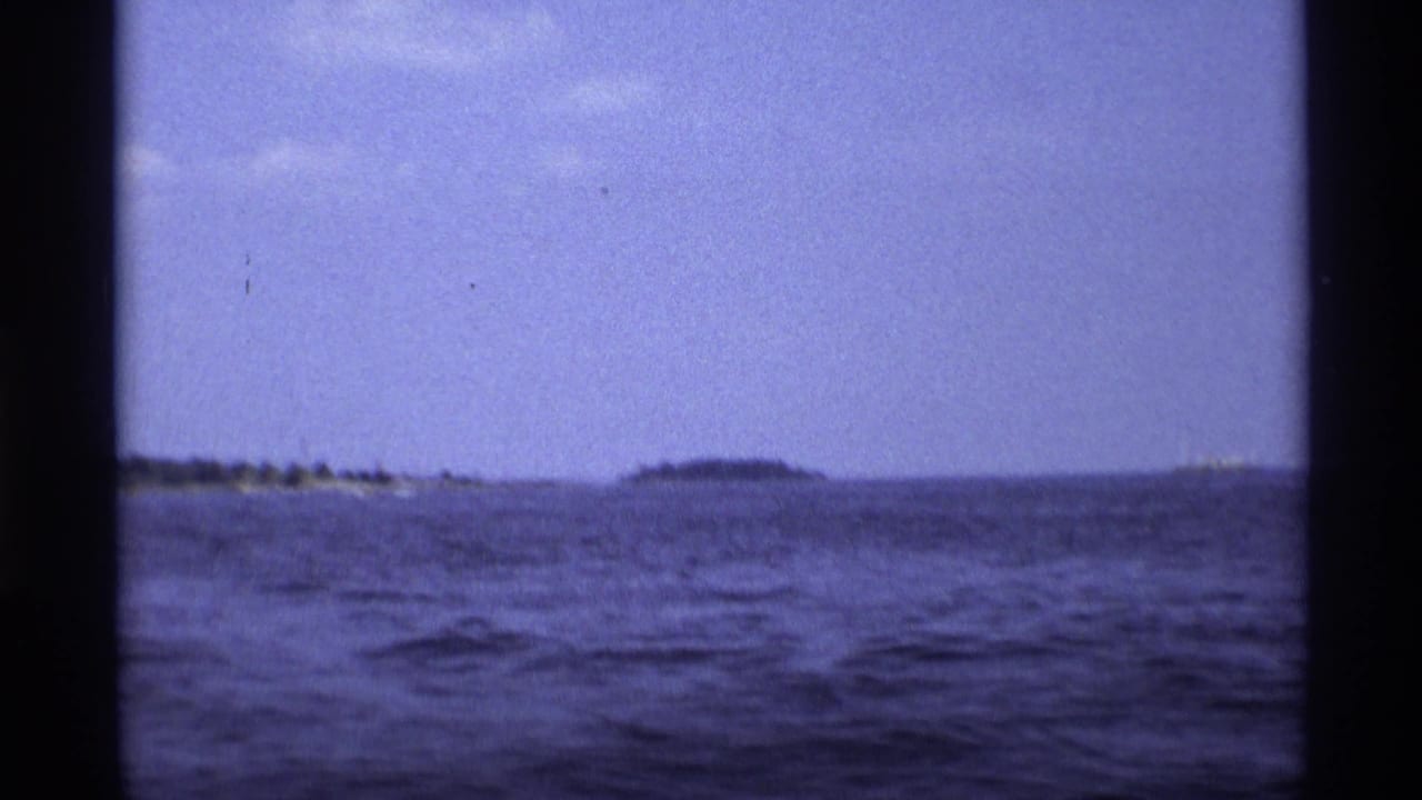 1973 New York 8mm frame looking across open water toward low distant land under a hazy blue-purple sky.