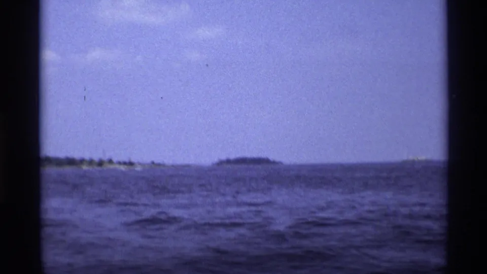 1973 New York 8mm frame looking across open water toward low distant land under a hazy blue-purple sky.