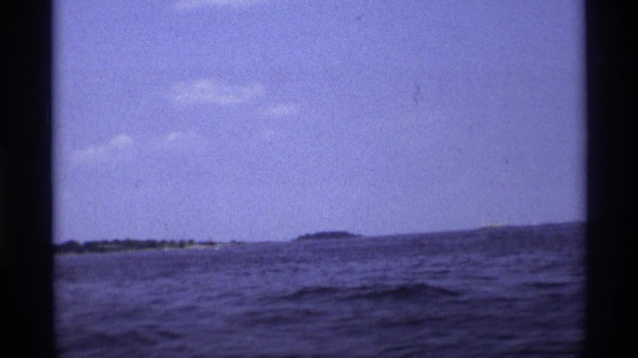 Open water and distant shoreline seen from a moving boat with dark film borders.