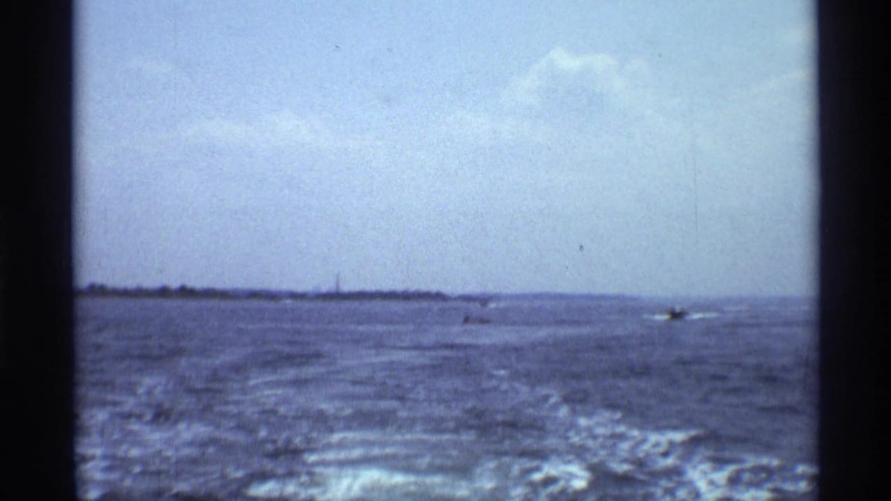 Wide 1973 New York lake view with wake trailing across the water and small boats near the distant shore.