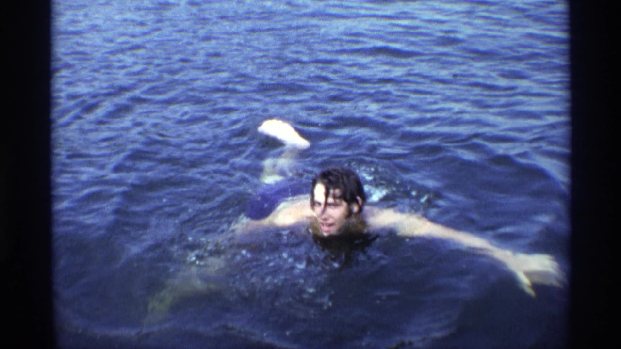 The young man swims closer to the camera, arms extended across the surface of deep blue water.