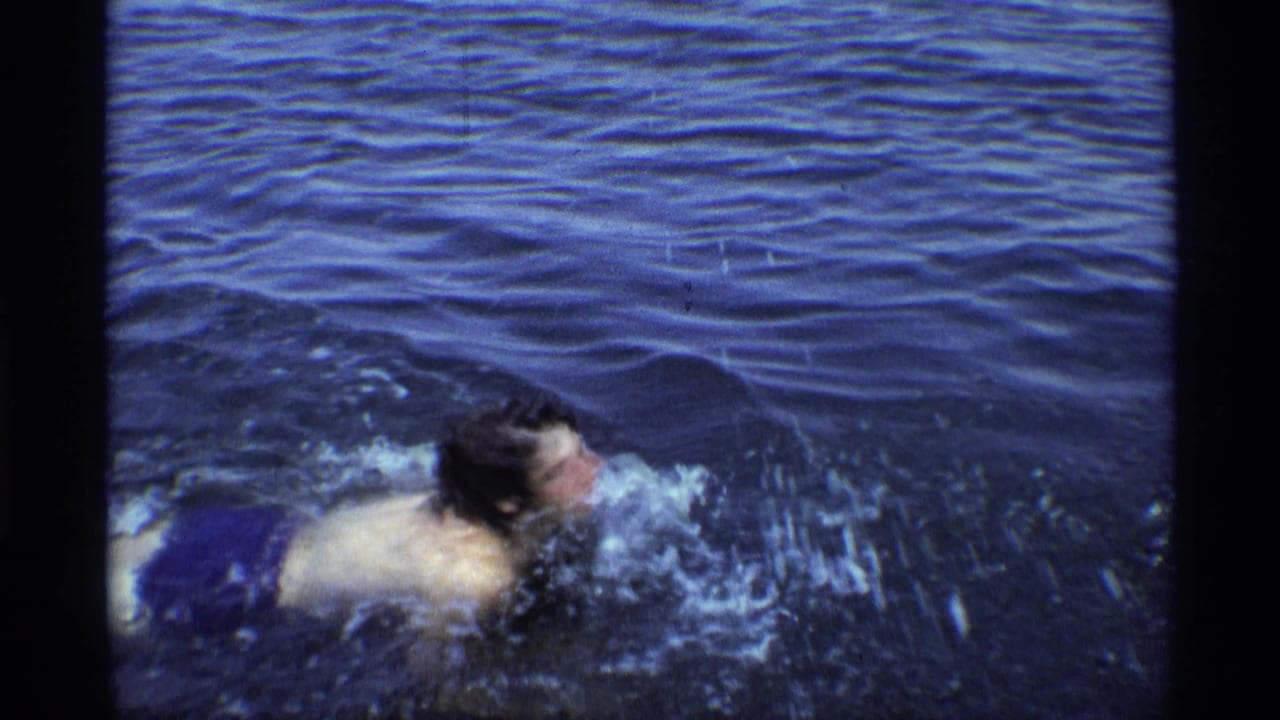The swimmer turns sideways in the water, creating splashes as handheld 8mm framing follows the movement.