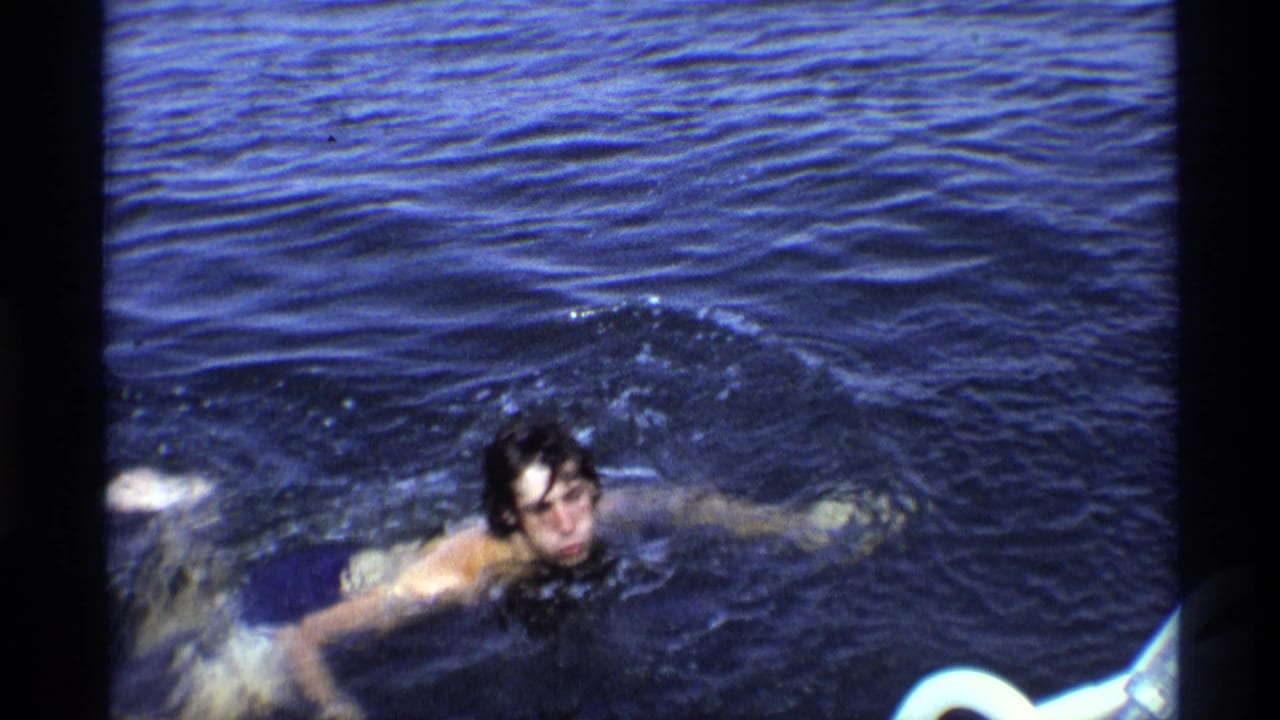 Young man swimming through dark blue water near the camera.