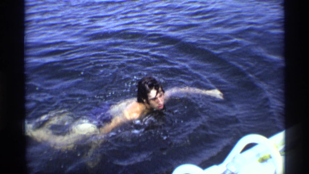 Dark-haired swimmer moves across deep blue water, with a white float or poolside object at the lower right.