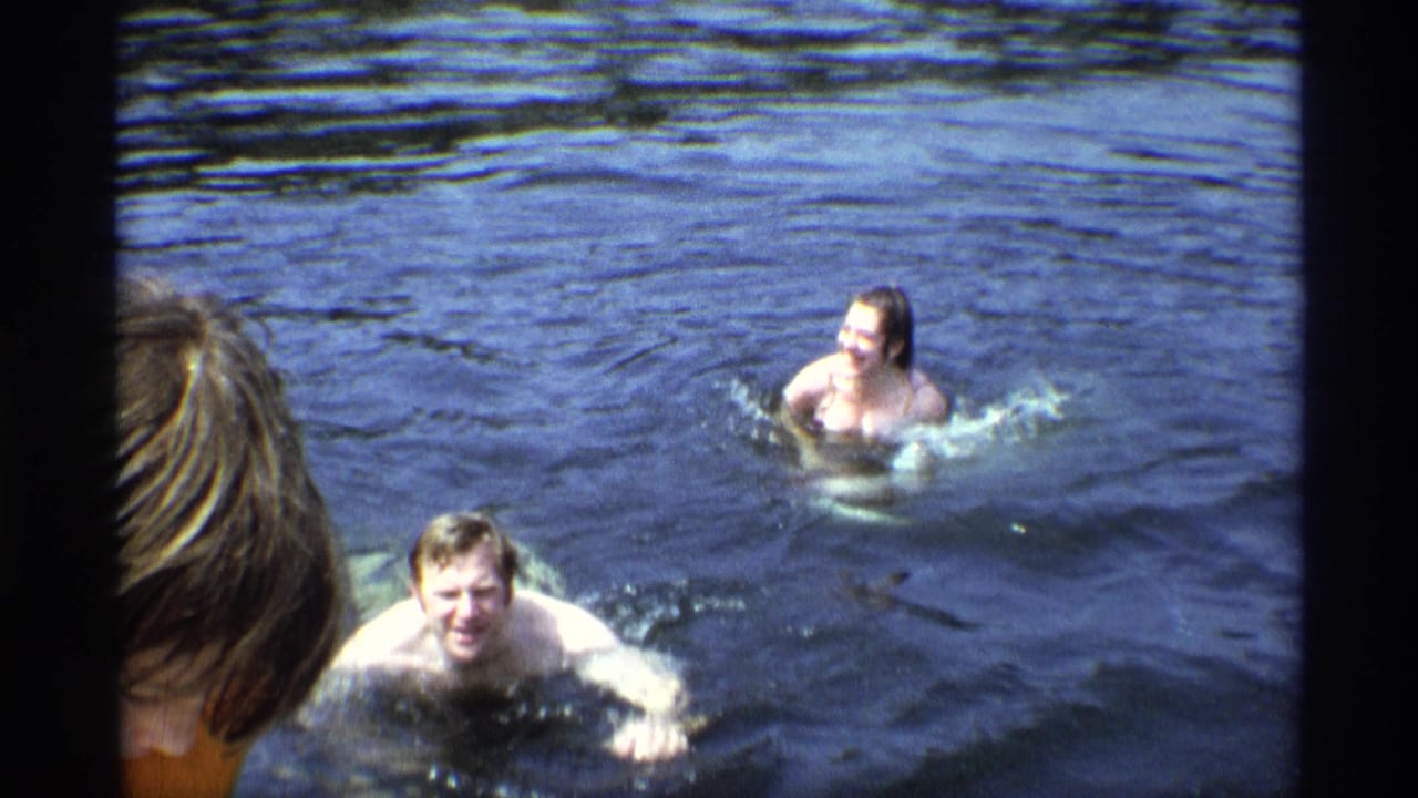Two swimmers in lake water with a person's head partly visible in the foreground.
