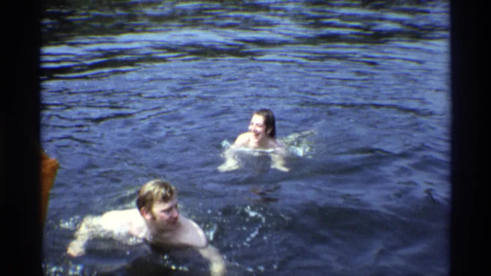 1973 New York 8mm frame showing two adults separated in the lake, both surrounded by rippling water and light splashes.