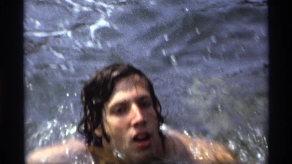 A long-haired man swims close to the camera as water churns around his shoulders in 1973 New York footage.