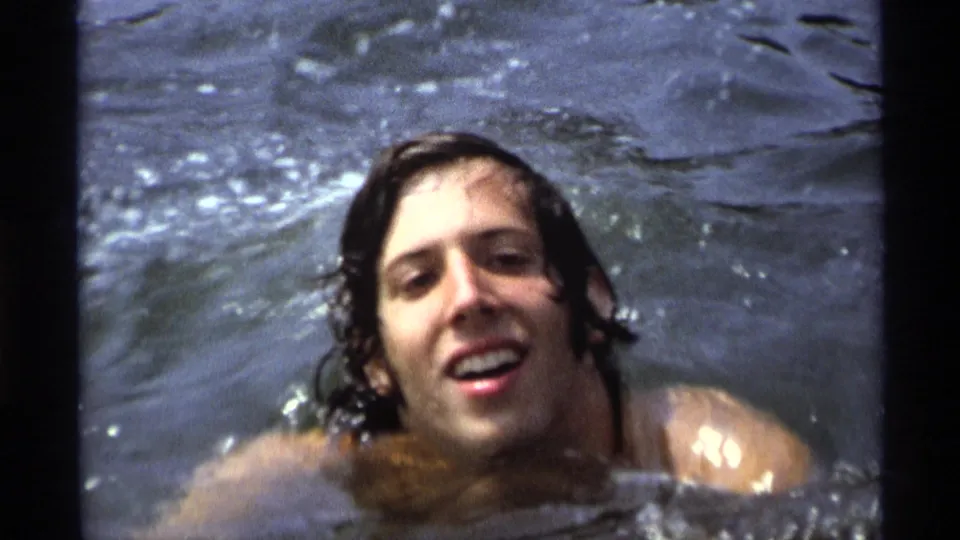 A wet-haired man smiles toward the camera while swimming in open water, consistent with the 1973 New York home-movie metadata.