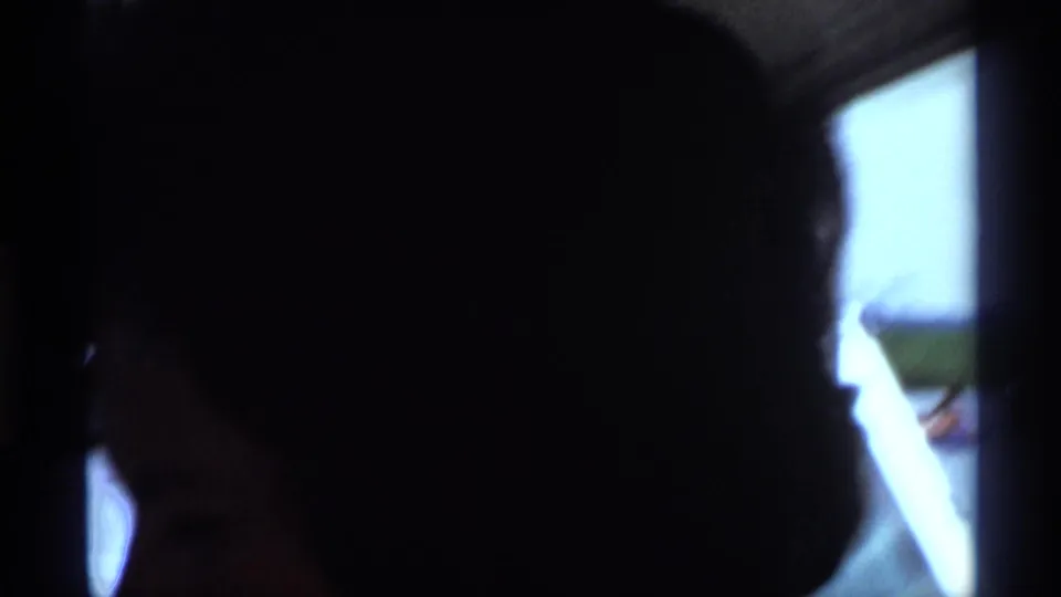A shadowed close-up of a woman in a bright-windowed interior, from 1973 New York 8mm home-movie footage.