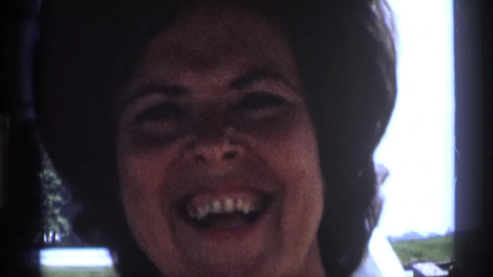 A close-up shows the woman laughing in shadowed interior light, consistent with the 1973 New York home-movie clip.