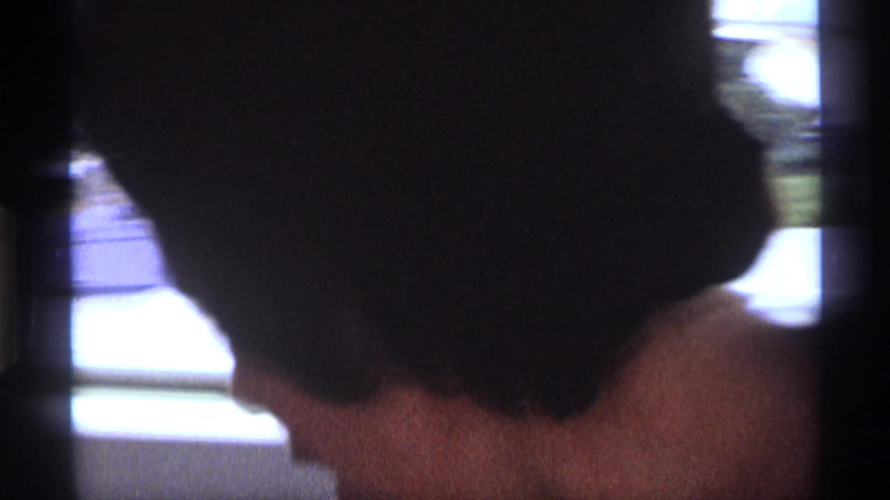 Back and side of a woman with dark styled hair near a bright window.