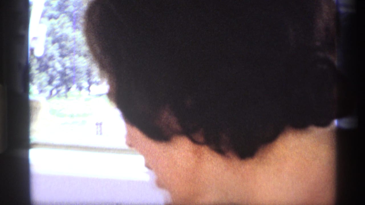 In this 1973 New York home-movie frame, the woman faces toward a window as greenery passes outside.