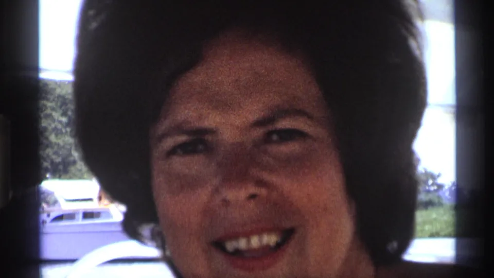 The woman smiles toward the camera inside the vehicle or boat, with daylight and outdoor shapes visible behind her.