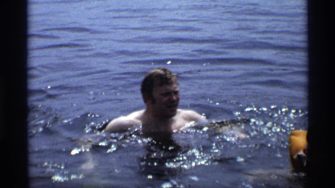 Adult man swims in open water in 1973 New York 8mm home-movie footage, with ripples and sun glints around him.