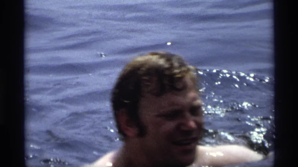 A soft, close handheld frame shows the man's face near the lower edge as he swims in rippling water.