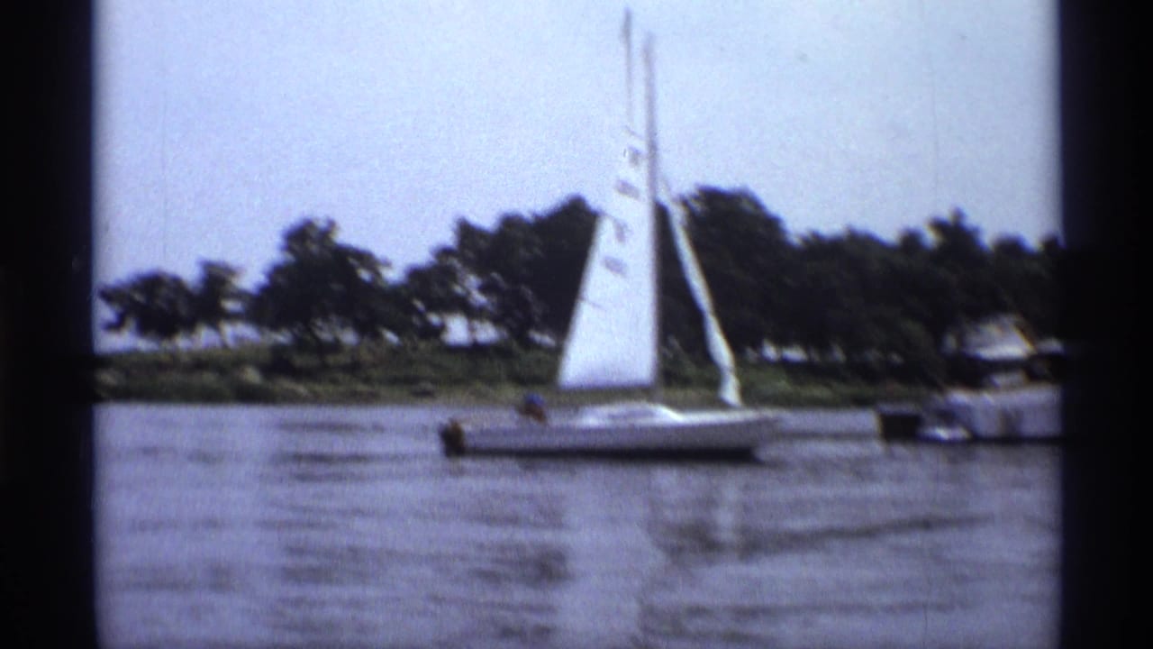 Small white sailboat on a calm New York lake in 1973, with a motorboat nearby and trees along the shore.