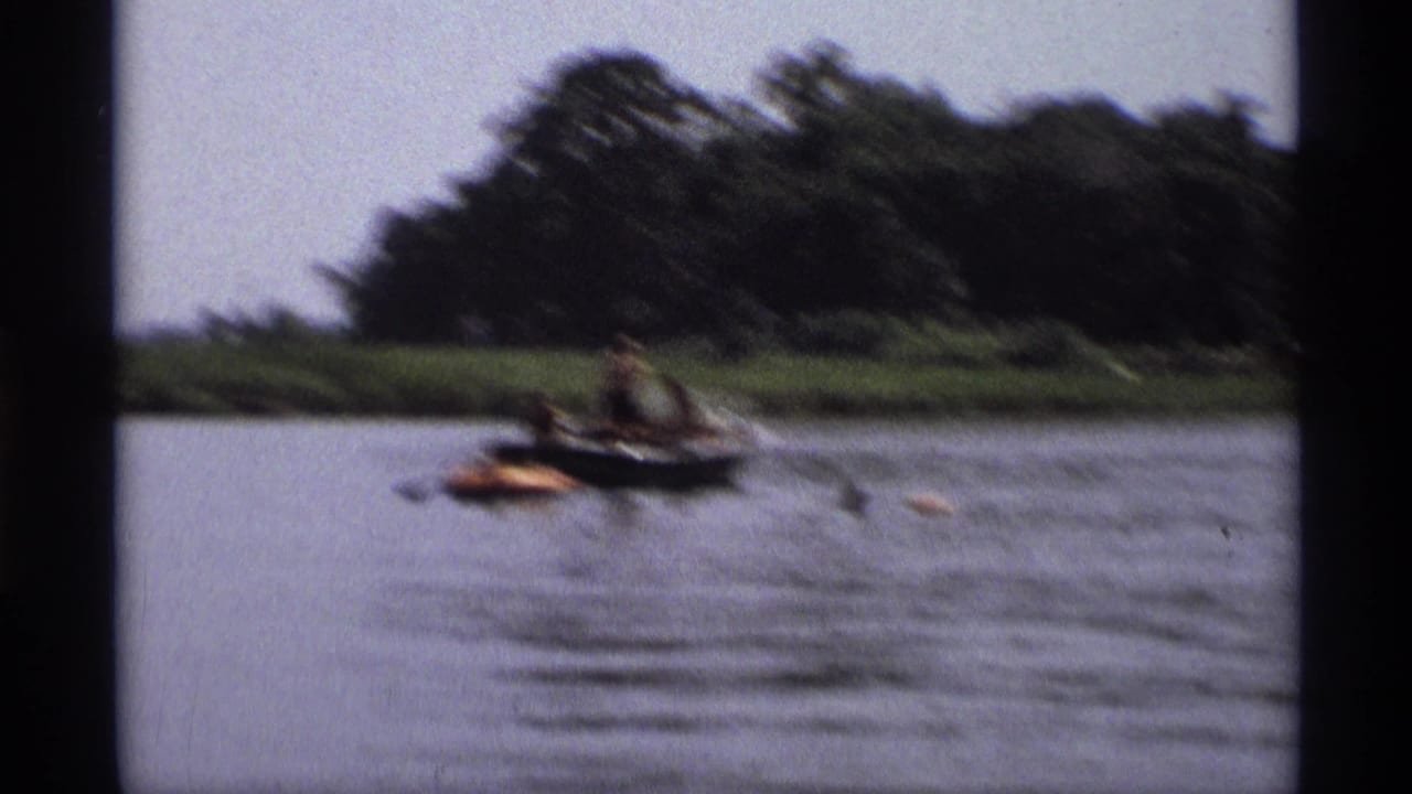 Small boat and orange raft on a calm lake with trees along the far shore.