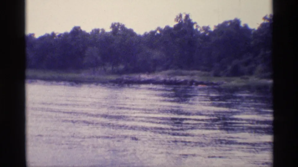 1973 New York 8mm frame showing rippling lake water and a wooded shoreline under a hazy sky.